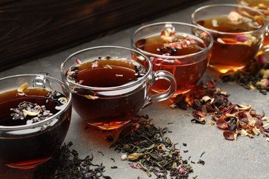 Photo of Aromatic herbal tea in glass cups and dry leaves on grey table, closeup