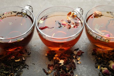 Photo of Aromatic herbal tea in glass cups and dry leaves on grey table, closeup