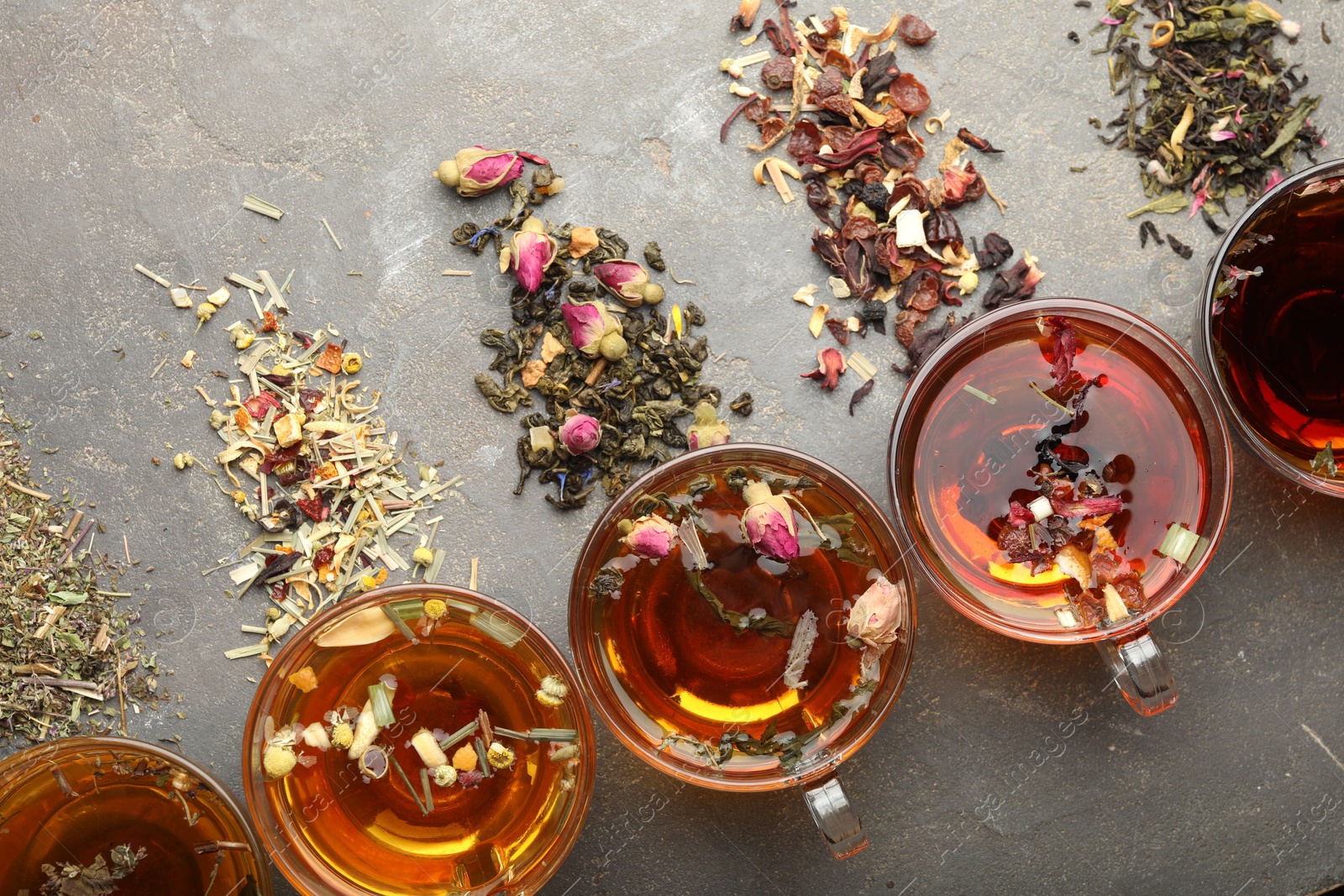 Aromatic herbal tea in glass cups, dry leaves and flowers on grey table, flat lay Photo of Aromatic herbal tea in glass cups, dry leaves and flowers on grey table, flat lay
