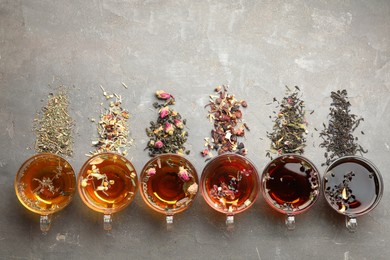 Photo of Aromatic herbal tea in glass cups, dry leaves and flowers on grey table, flat lay. Space for text