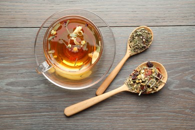 Photo of Aromatic herbal tea in glass cup and dry leaves on wooden table, flat lay
