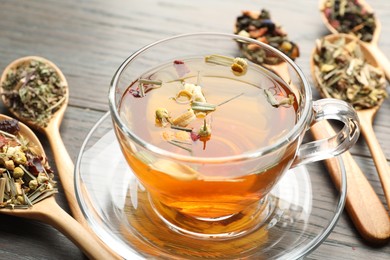 Photo of Aromatic herbal tea in glass cup and dry leaves on wooden table, closeup