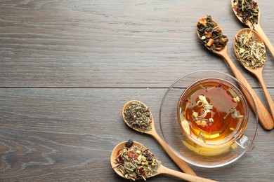 Photo of Aromatic herbal tea in glass cup and dry leaves on wooden table, flat lay. Space for text
