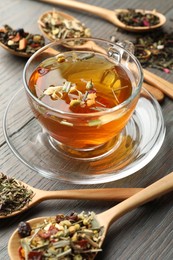 Photo of Aromatic herbal tea in glass cup and dry leaves on wooden table, closeup