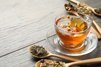 Photo of Aromatic herbal tea in glass cup and dry leaves on wooden table, closeup. Space for text