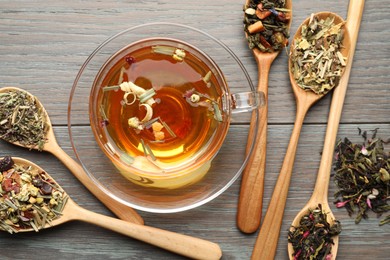 Photo of Aromatic herbal tea in glass cup and dry leaves on wooden table, flat lay