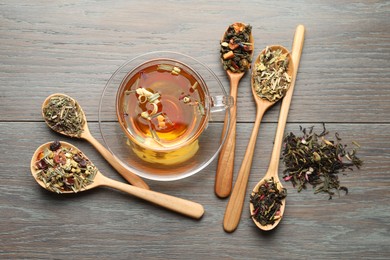 Photo of Aromatic herbal tea in glass cup and dry leaves on wooden table, flat lay