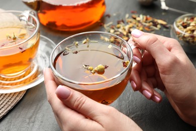 Photo of Woman with aromatic herbal tea at black table, closeup