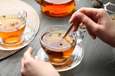 Photo of Woman with aromatic herbal tea at black table, closeup