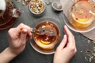 Photo of Woman with aromatic herbal tea at black table, top view