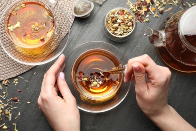 Photo of Woman with aromatic herbal tea at black table, top view