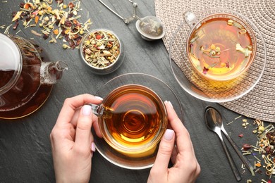 Photo of Woman with aromatic herbal tea at black table, top view