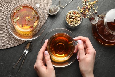 Photo of Woman with aromatic herbal tea at black table, top view