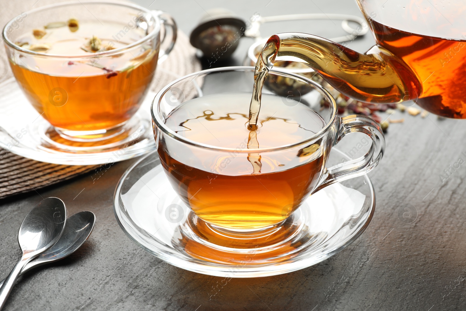 Pouring herbal tea from teapot into cup at black table, closeup Photo of Pouring herbal tea from teapot into cup at black table, closeup