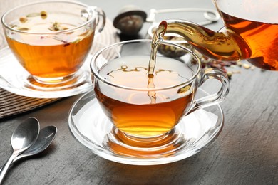 Photo of Pouring herbal tea from teapot into cup at black table, closeup
