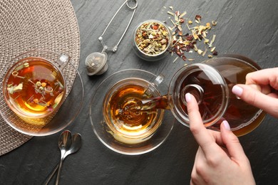 Photo of Woman pouring herbal tea from teapot into cup at black table, top view