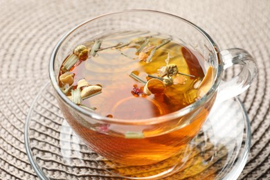 Photo of Aromatic herbal tea in glass cup on mat, closeup
