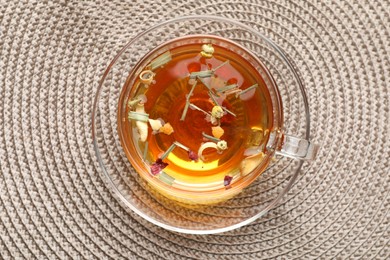Photo of Aromatic herbal tea in glass cup on mat, top view