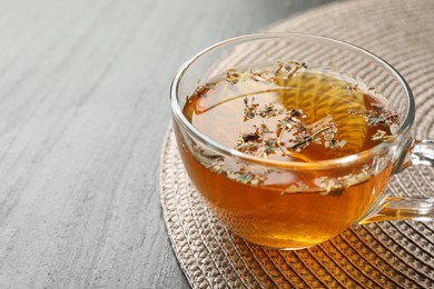 Photo of Aromatic herbal tea in glass cup on black table, closeup. Space for text