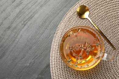 Photo of Aromatic herbal tea in glass cup and spoon on black table, top view. Space for text