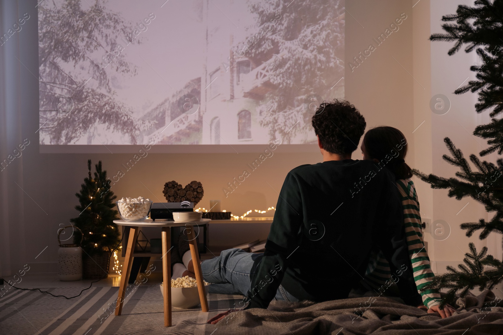 Couple watching Christmas movie via video projector at home, back view Photo of Couple watching Christmas movie via video projector at home, back view