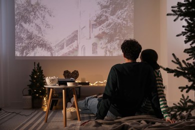 Photo of Couple watching Christmas movie via video projector at home, back view