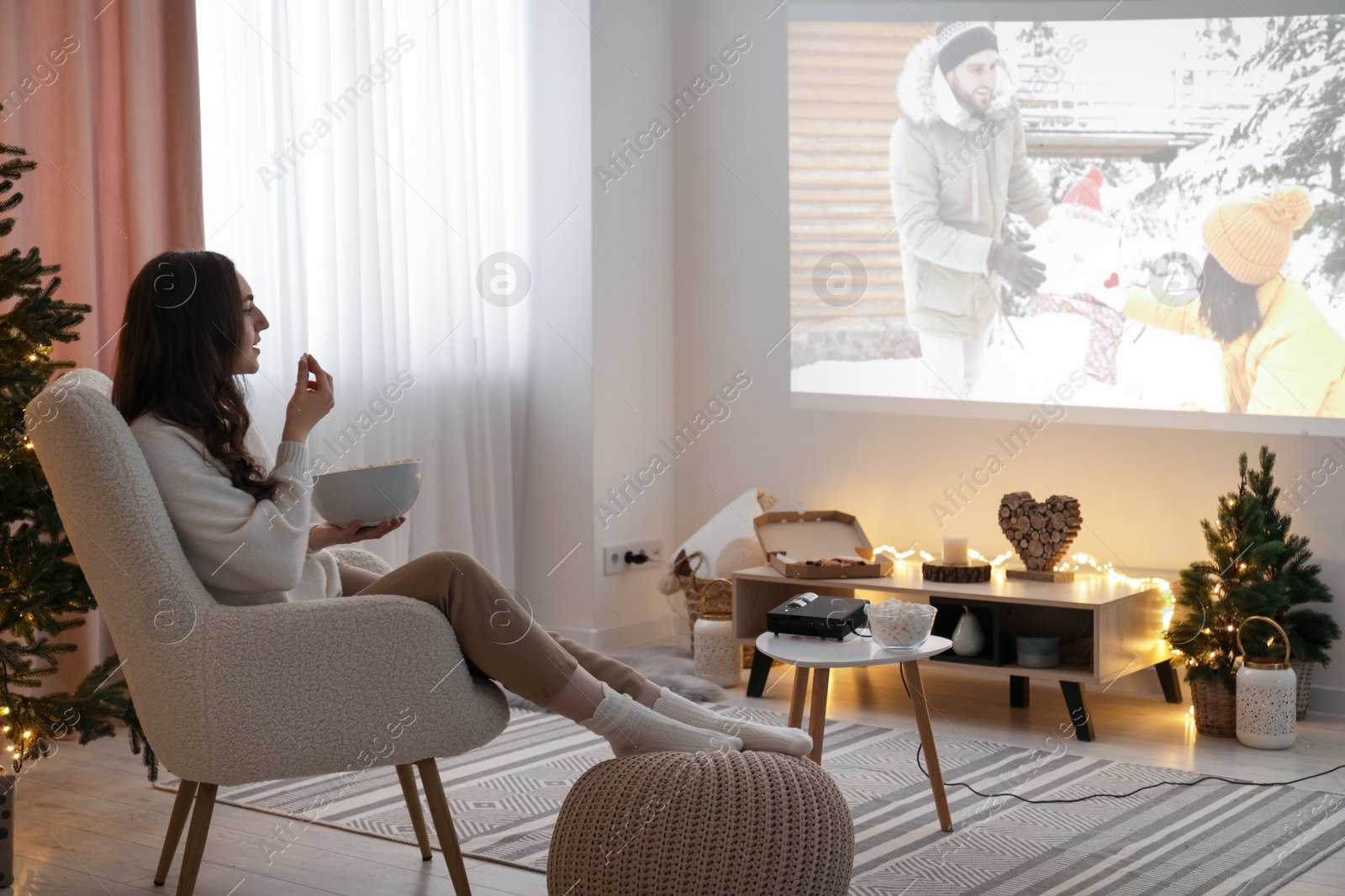 Woman with popcorn watching romantic Christmas movie via video projector at home Photo of Woman with popcorn watching romantic Christmas movie via video projector at home