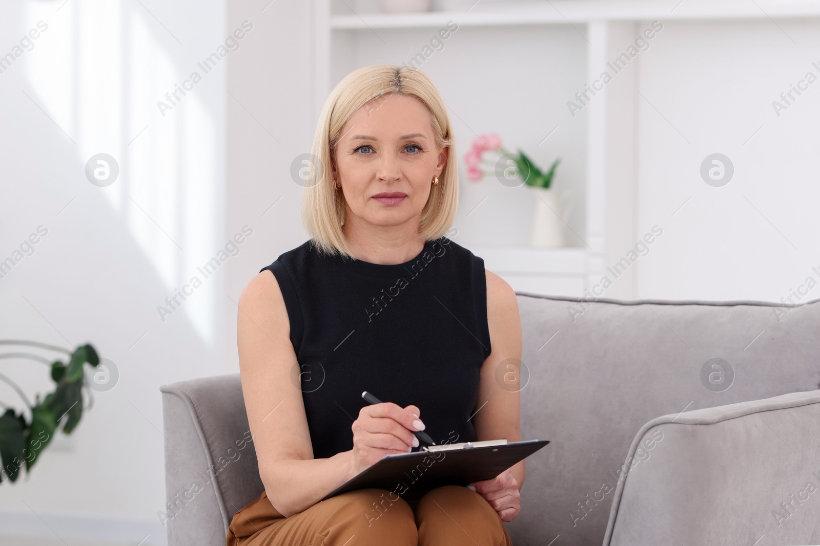 Professional psychologist with clipboard and pen in armchair indoors Photo of Professional psychologist with clipboard and pen in armchair indoors