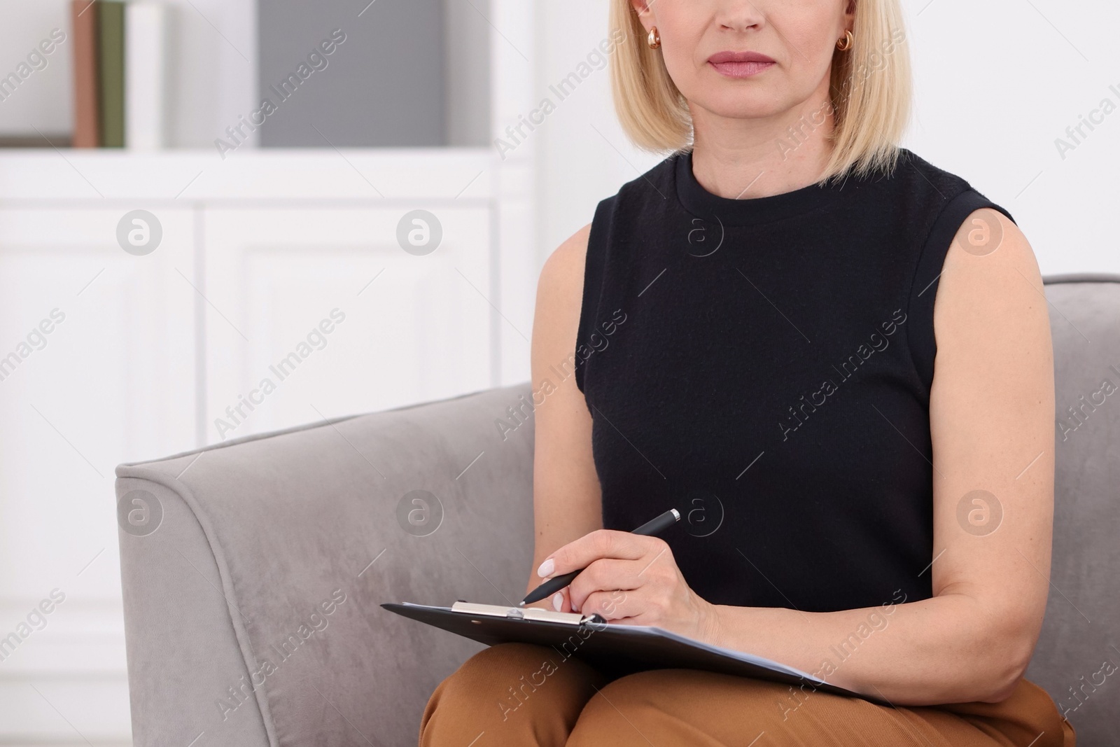 Professional psychologist with clipboard and pen in armchair indoors, closeup Photo of Professional psychologist with clipboard and pen in armchair indoors, closeup