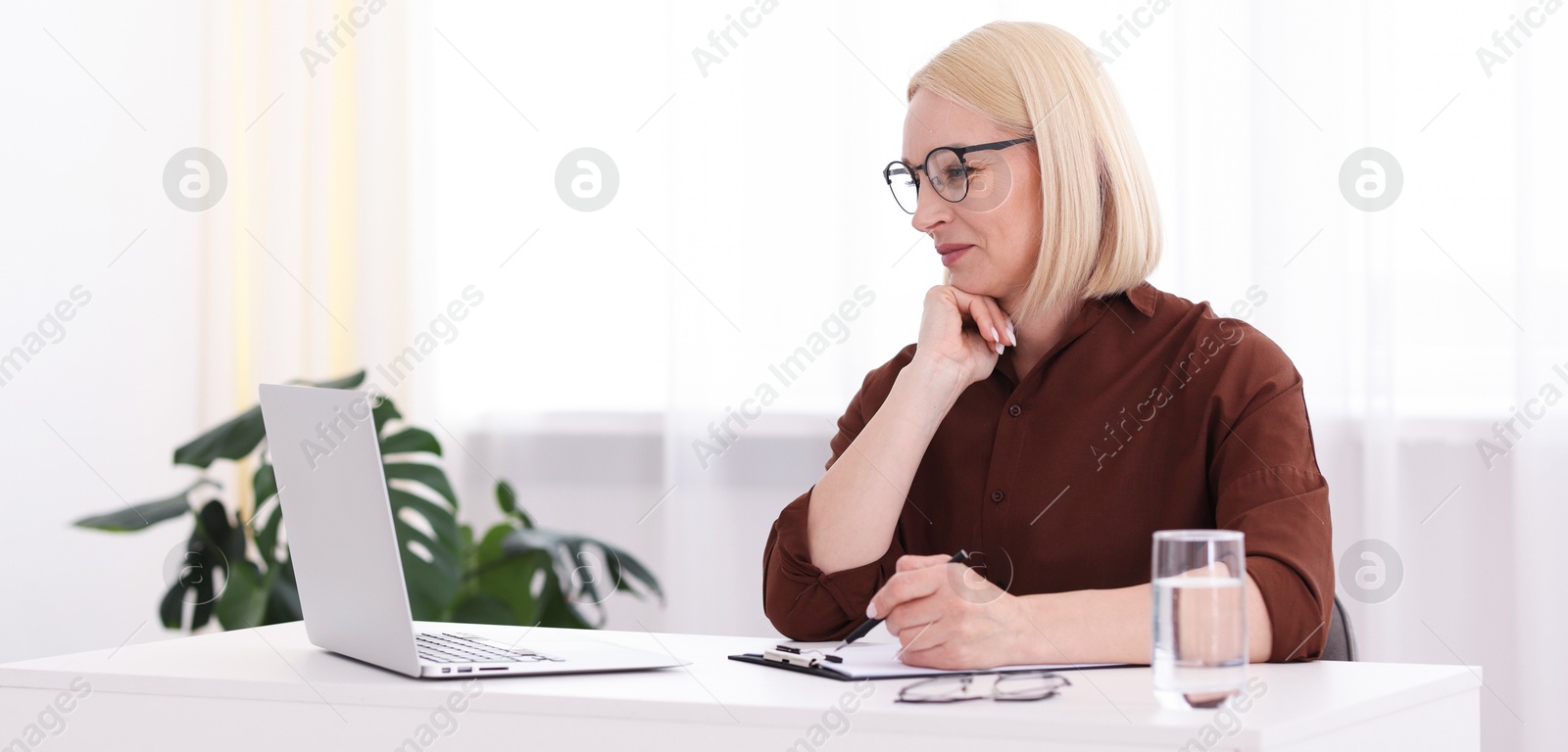 Professional psychologist taking notes while working with laptop at table in office Photo of Professional psychologist taking notes while working with laptop at table in office