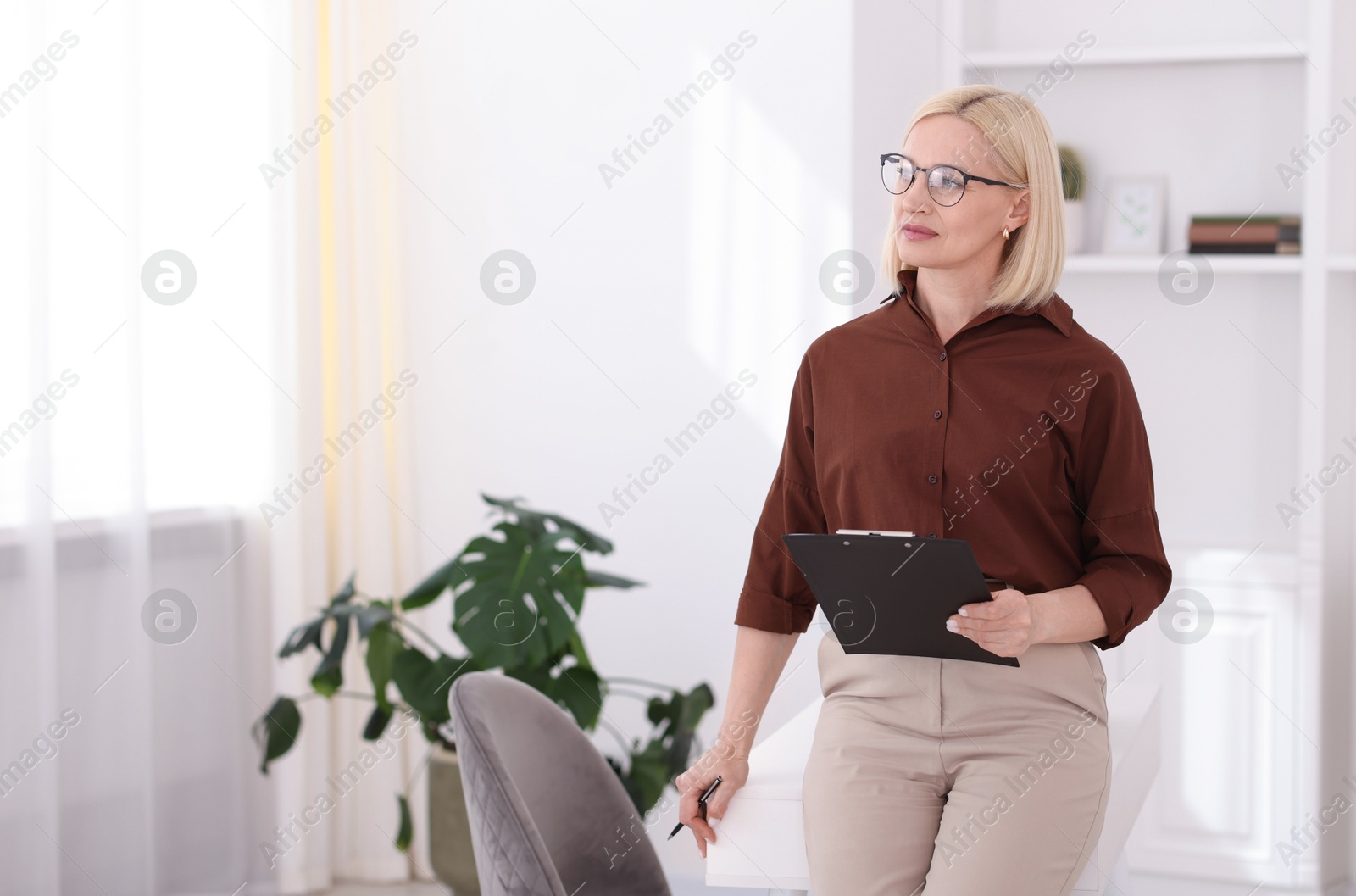 Professional psychologist with clipboard near table in office, space for text Photo of Professional psychologist with clipboard near table in office, space for text