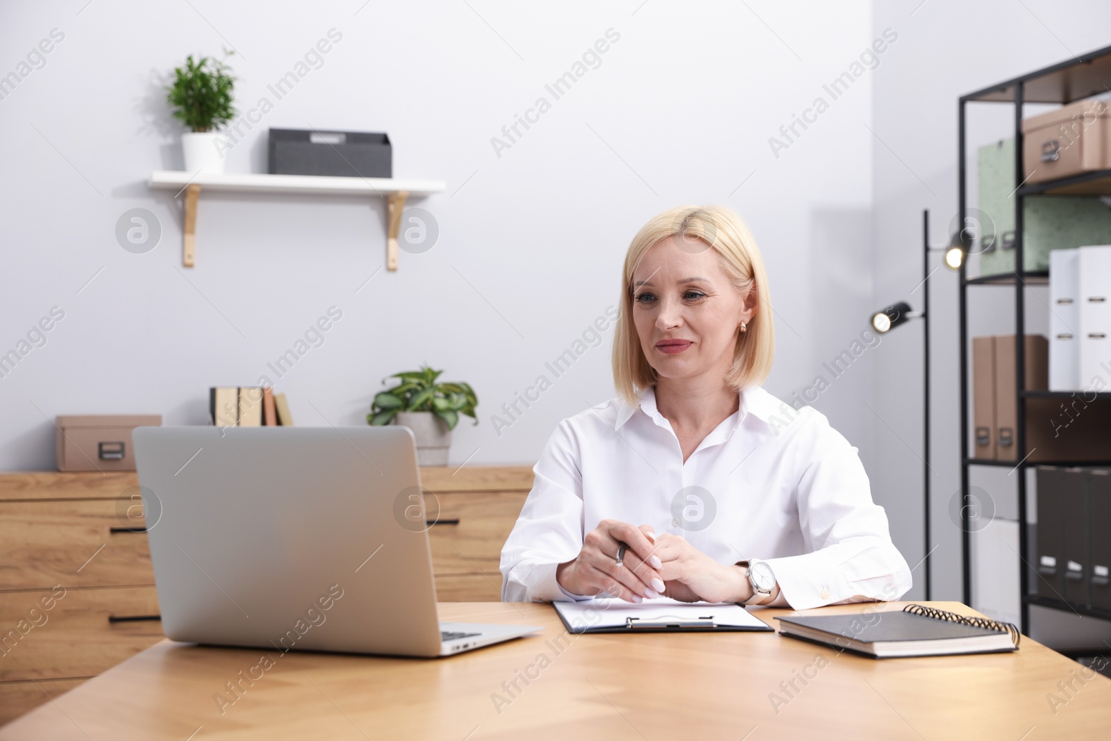 Professional psychologist taking notes while working with laptop at table in office Photo of Professional psychologist taking notes while working with laptop at table in office