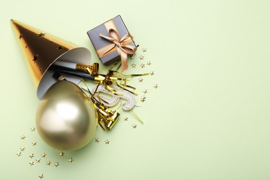 Photo of Party hat, blowers, gift box and confetti on light green background, flat lay. Space for text