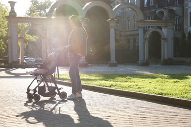 Photo of Mother walking with her baby in stroller at park on sunny day. Space for text