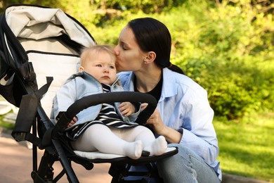 Photo of Mother kissing her cute baby in stroller at park