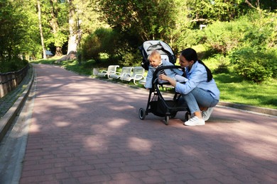 Photo of Mother with her cute baby in stroller looking at bird outdoors