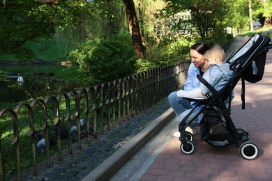 Photo of Mother with her cute baby in stroller looking at birds outdoors
