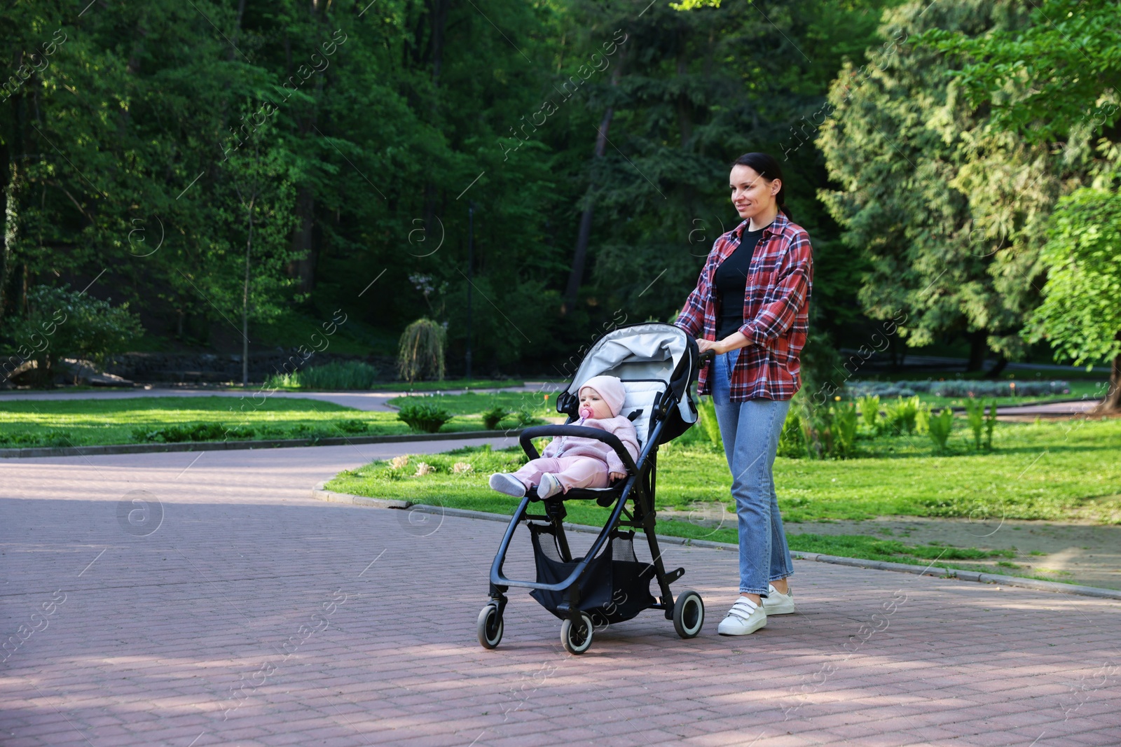 Photo of Mother walking with her baby in stroller at park. Space for text