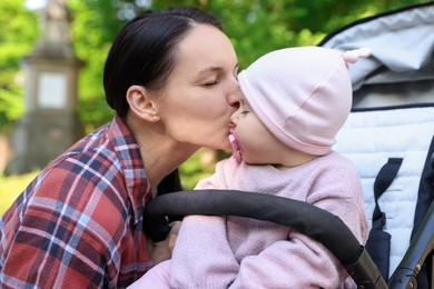 Photo of Mother kissing her cute baby in stroller at park