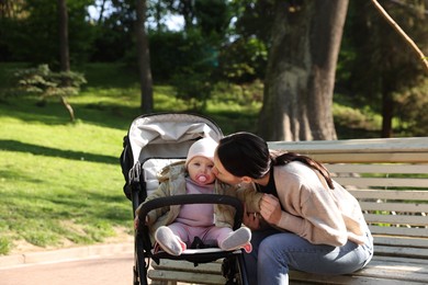 Photo of Mother kissing her cute baby in stroller at park