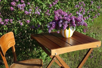 Photo of Beautiful lilac flowers in vase on wooden table in garden