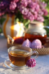 Photo of Beautiful lilac flowers, tea and zephyrs on table in garden, closeup