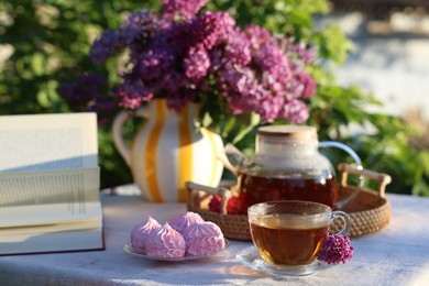 Photo of Beautiful lilac flowers, tea, zephyrs and book on table in garden