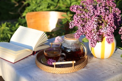 Photo of Beautiful lilac flowers, tea and book on table in garden