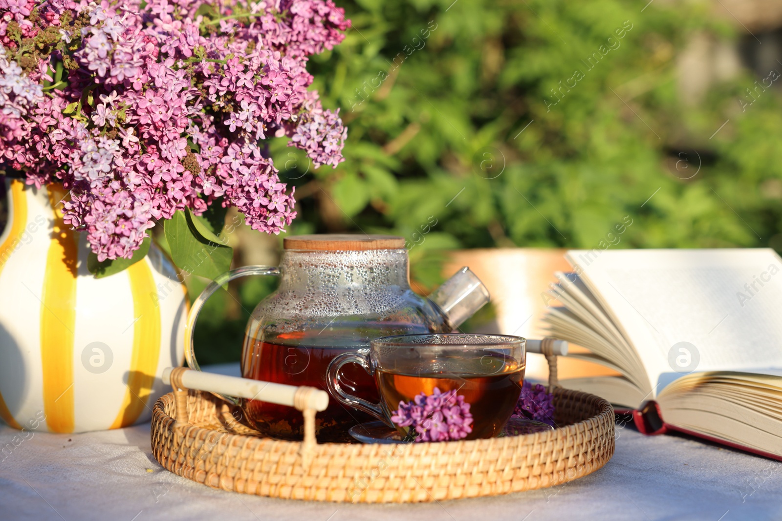 Beautiful lilac flowers, tea and book on table in garden, closeup Photo of Beautiful lilac flowers, tea and book on table in garden, closeup