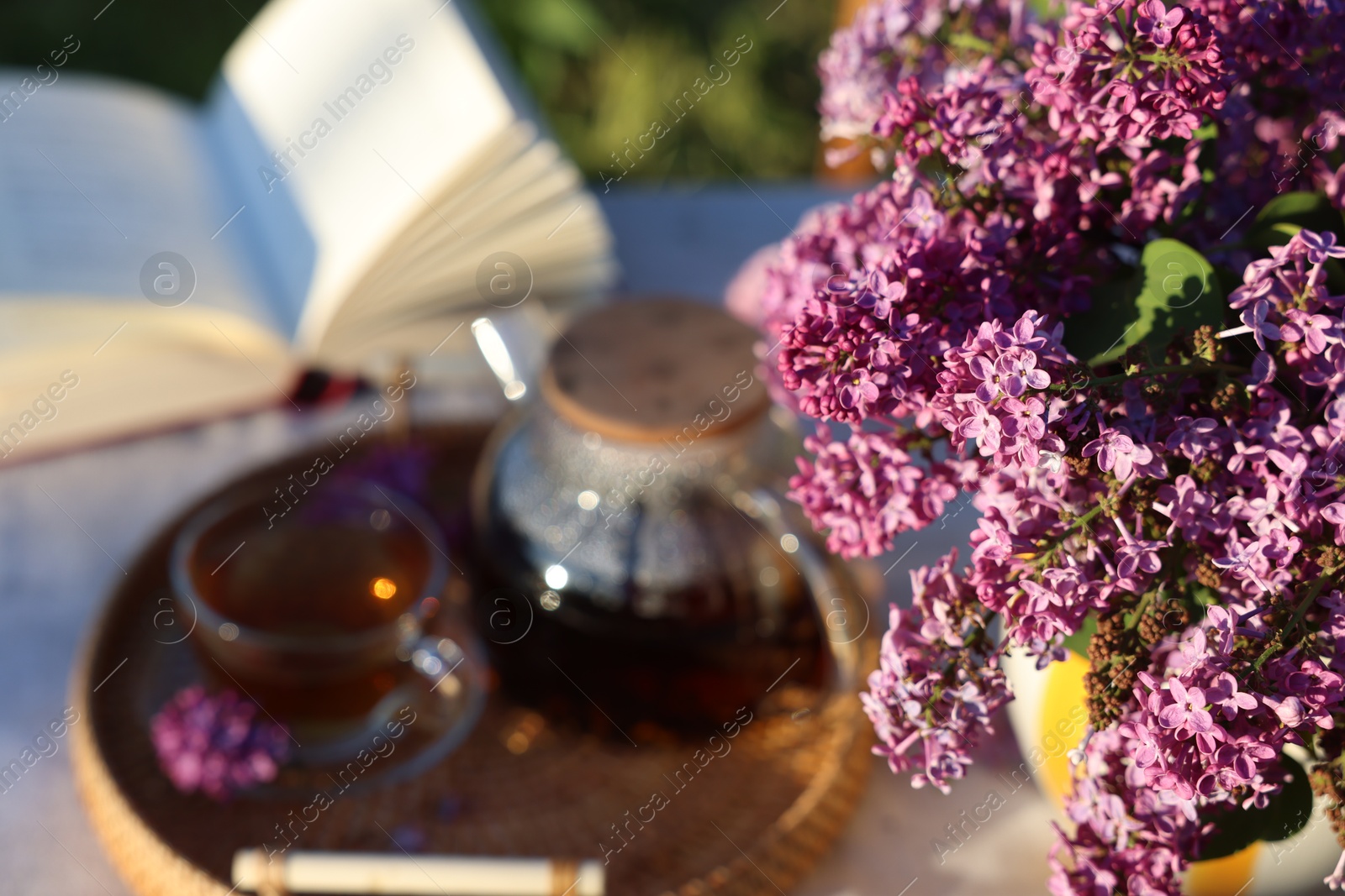 Beautiful lilac flowers, tea and book on table in garden, closeup Photo of Beautiful lilac flowers, tea and book on table in garden, closeup