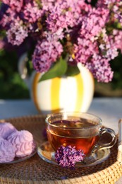 Photo of Beautiful lilac flowers, tea and zephyrs on table in garden, closeup