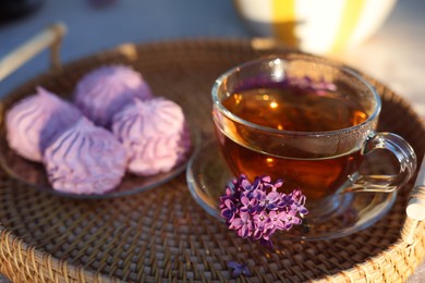Photo of Beautiful lilac flowers, tea and zephyrs on table in garden, closeup
