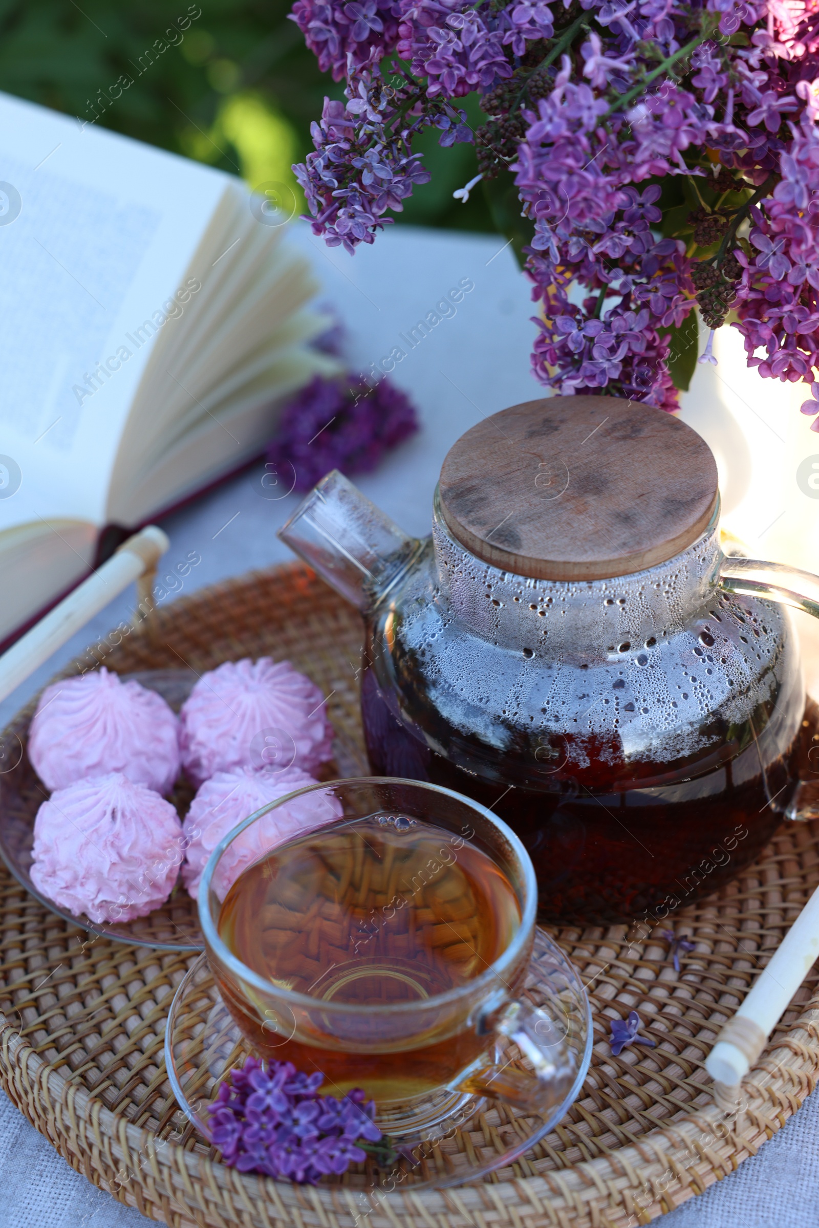 Beautiful lilac flowers, tea, zephyrs and book on table in garden, closeup Photo of Beautiful lilac flowers, tea, zephyrs and book on table in garden, closeup