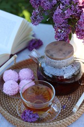 Photo of Beautiful lilac flowers, tea, zephyrs and book on table in garden, closeup